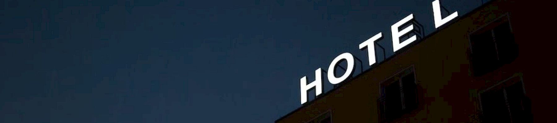 A building's façade with a "HOTEL" sign lit up at night against a dark blue sky.