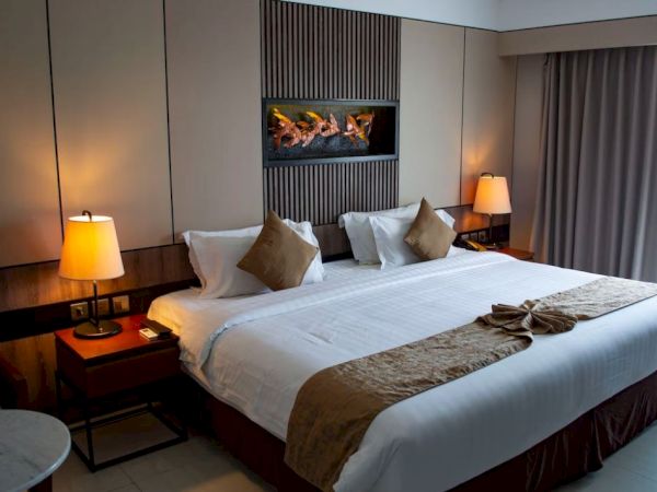 A cozy hotel room with a large bed, decorative pillows, bedside lamps, and a window with curtains, creating a welcoming atmosphere.