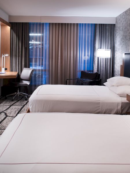 A hotel room with two beds, a wall-mounted TV, a desk with a chair, and modern decor.