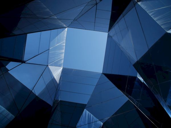 Geometric architecture with reflective glass surfaces and a central opening revealing blue sky.