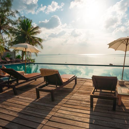 A serene poolside scene with lounge chairs, umbrellas, and a stunning ocean view, under a bright sky with clouds softly illuminated by the sun.