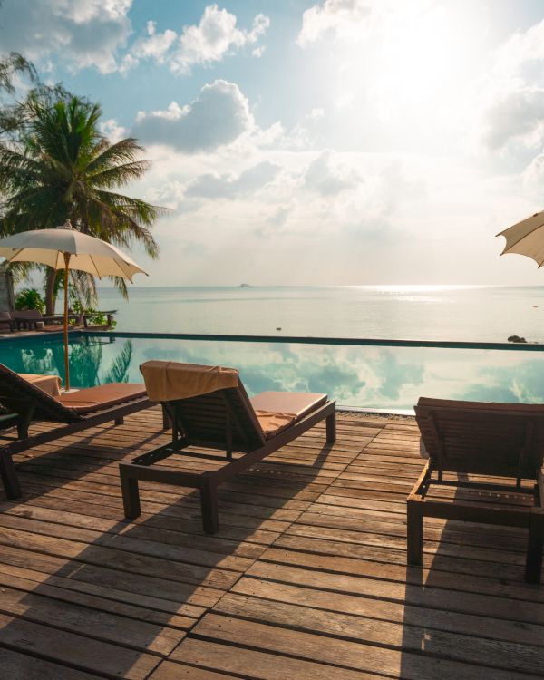 A serene poolside scene with lounge chairs, umbrellas, and a stunning ocean view, under a bright sky with clouds softly illuminated by the sun.