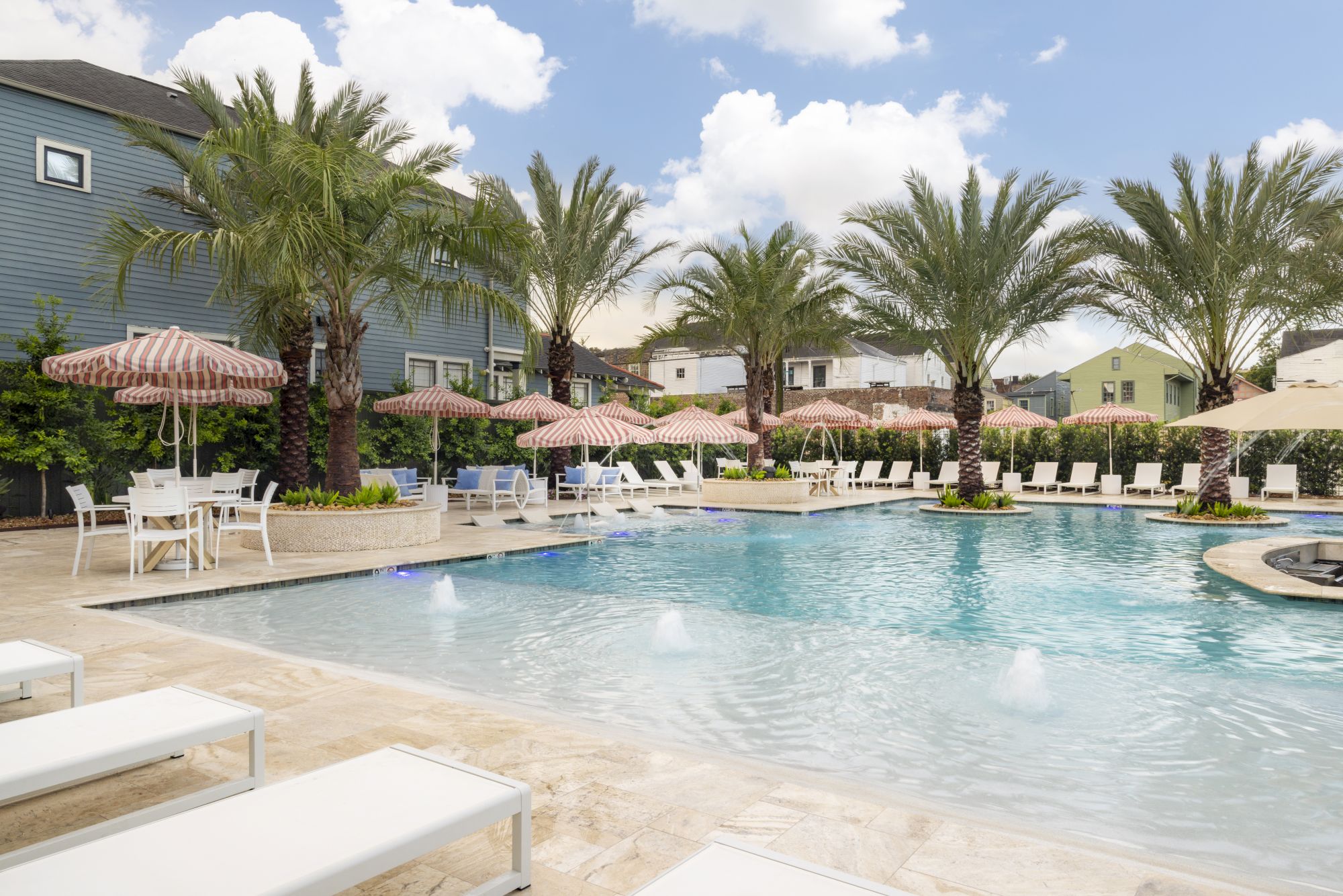 A serene pool area with lounge chairs, palm trees, and umbrellas creates an inviting outdoor space under a clear blue sky.