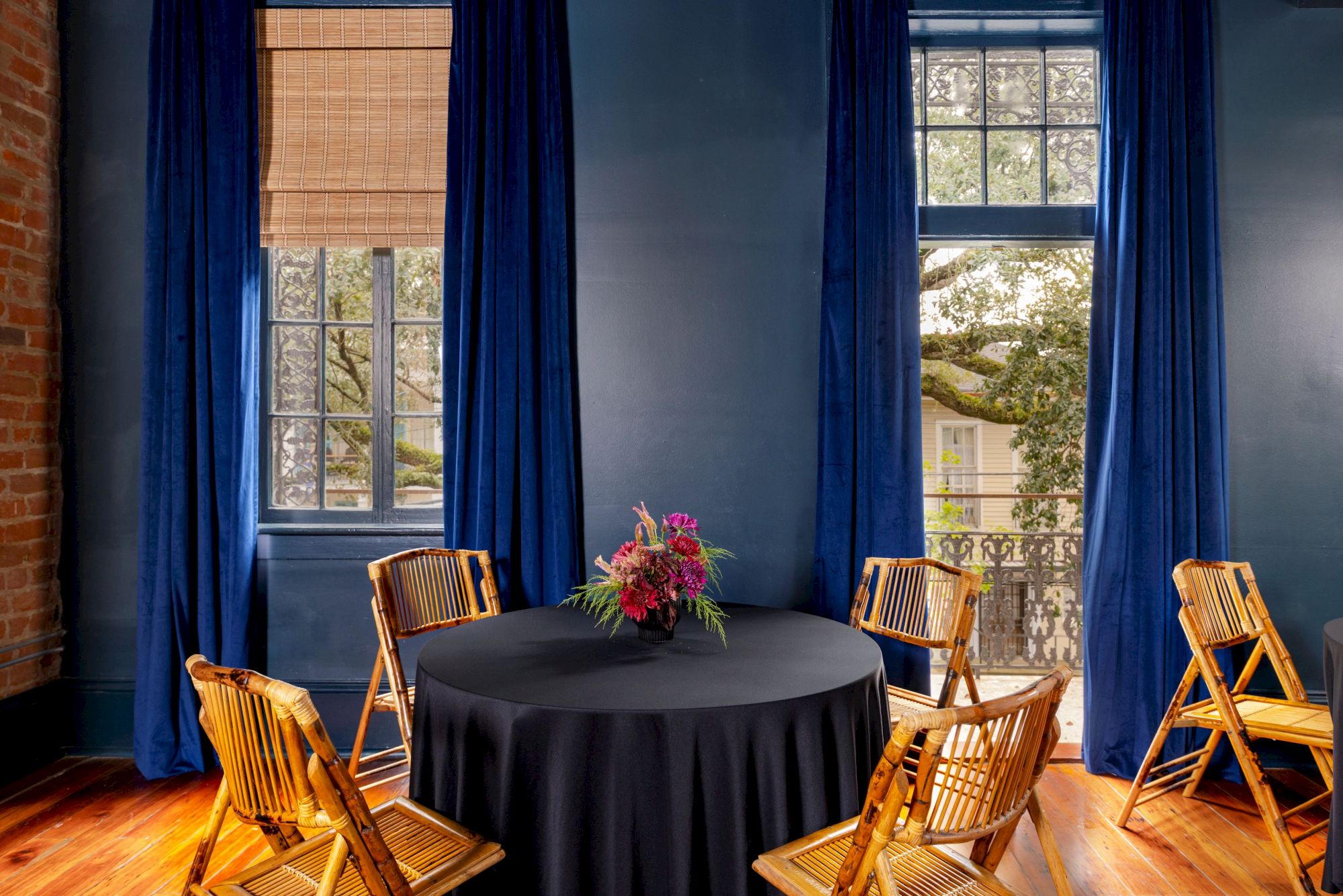 The image shows a room with blue walls, a round table with a black tablecloth, wooden chairs, and a floral centerpiece.