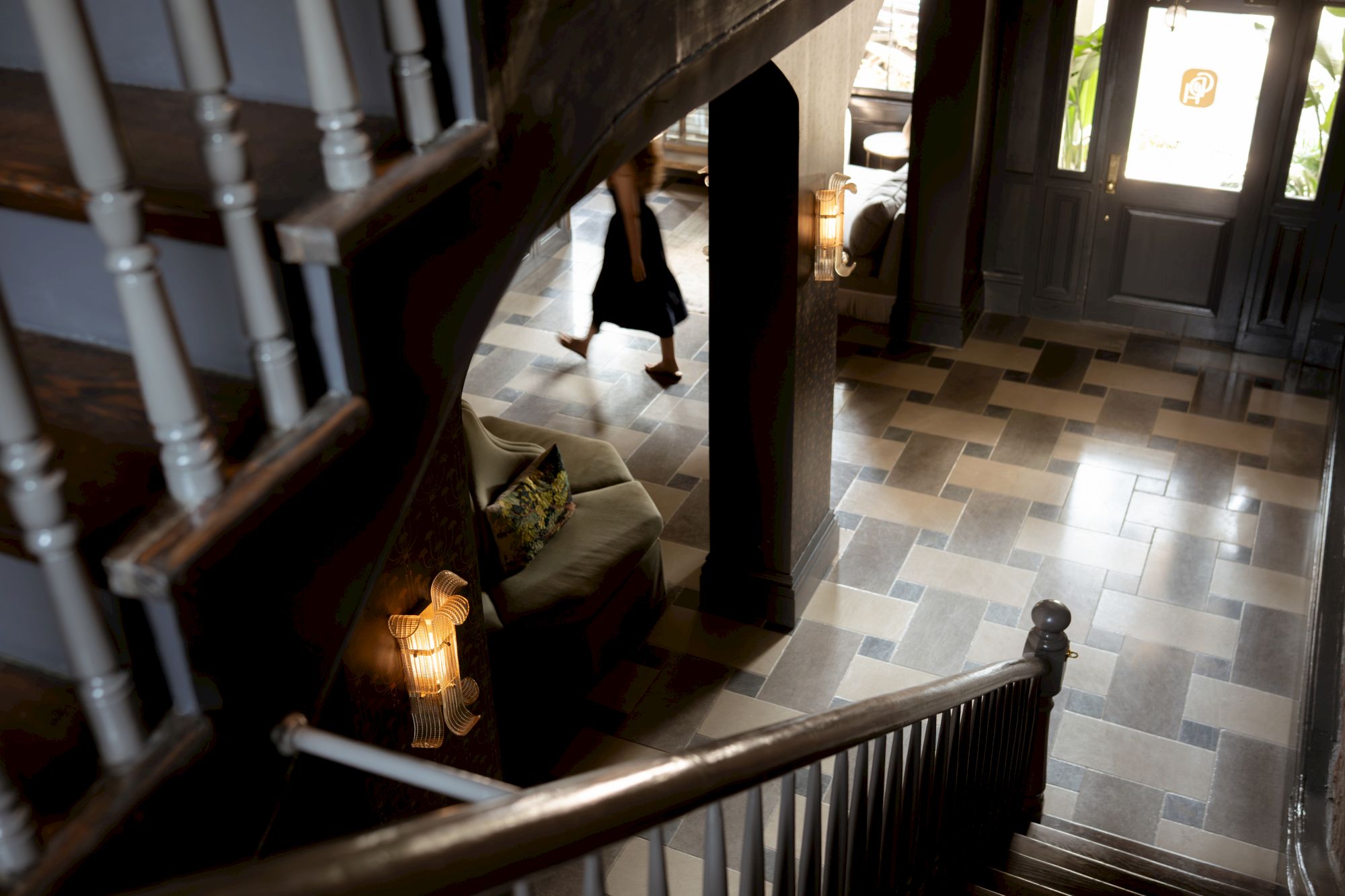 A person walks through a stylish foyer with a staircase, patterned floor, and ambient lighting.
