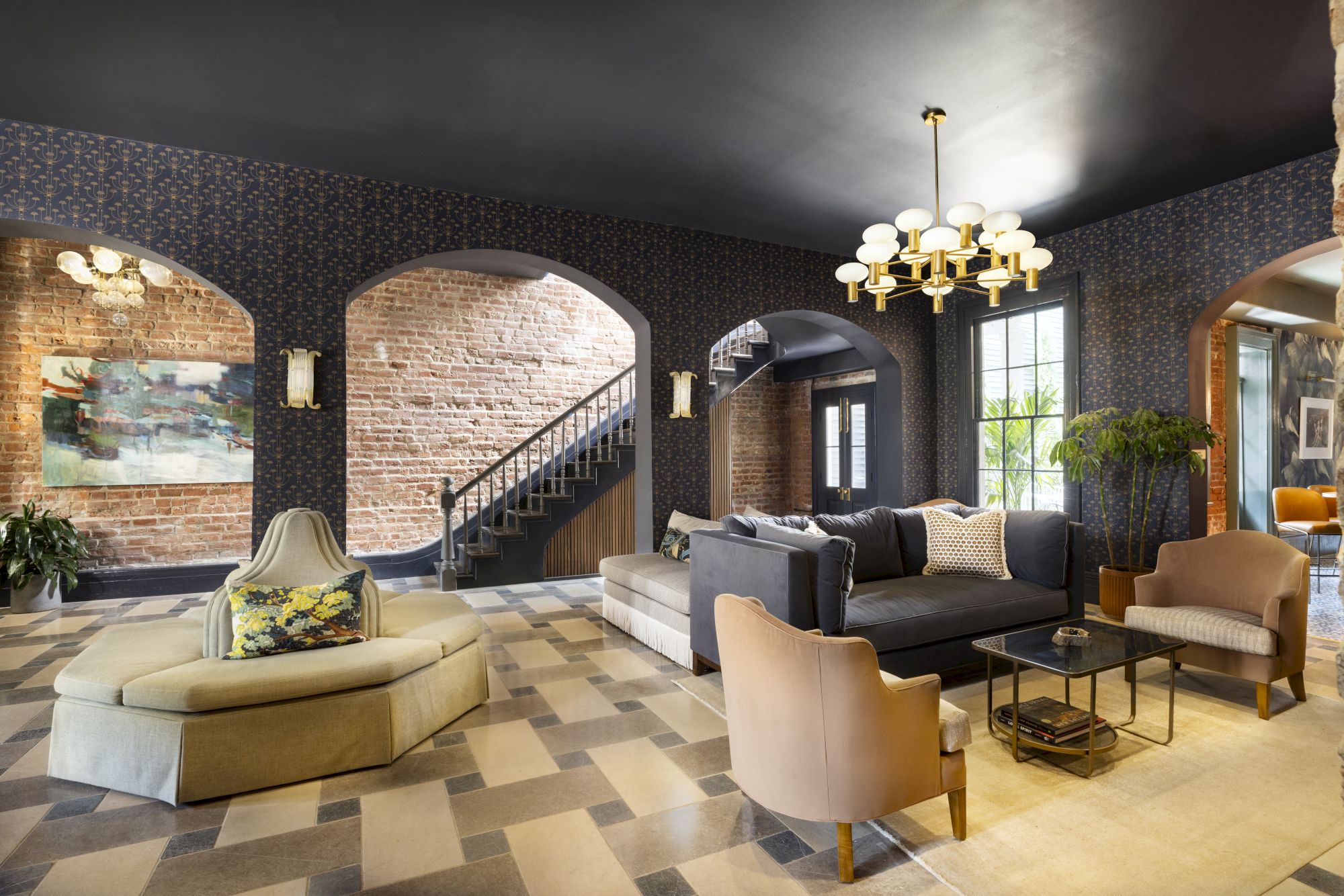 A stylish living room features modern furniture, a chandelier, and patterned flooring, with a staircase in the background.