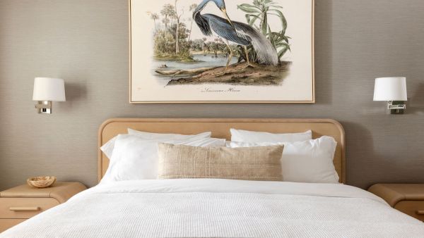 A cozy bedroom with a neatly made bed, flanked by two nightstands and wall lamps, featuring a framed bird illustration above.