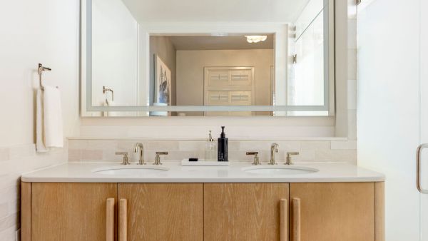 A bathroom with a large mirror, double sink vanity with wooden cabinets, and a towel hanging on the wall completes the decor.