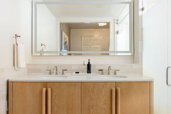 A bathroom with a large mirror, double sink vanity with wooden cabinets, and a towel hanging on the wall completes the decor.