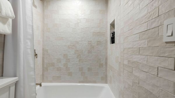 The image shows a bathroom with a bathtub, white curtain, and beige tiled walls. There's a small recessed shelf in the shower area.