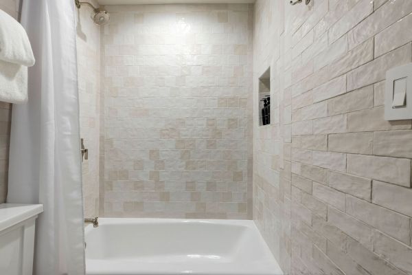 A bathroom with a white bathtub and shower curtain, tiled walls, a towel rack, and an inset shelf for toiletries is shown.
