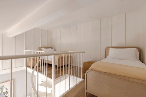 The image shows a cozy loft bedroom with two single beds, white walls, and a railing overlooking a staircase.