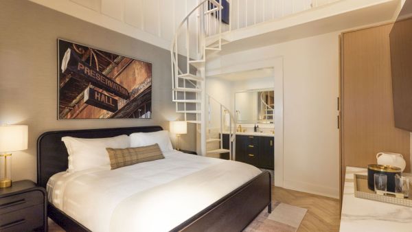 A modern bedroom with a spiral staircase leading to a loft, featuring a double bed and a painting on the wall.