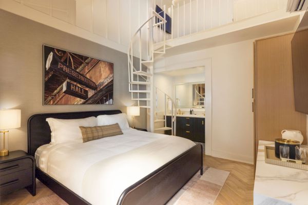 A modern bedroom with a spiral staircase leading to a loft, featuring a double bed and a painting on the wall.