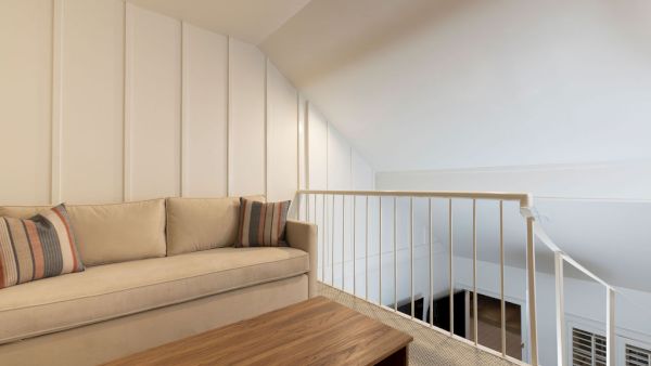 A cozy loft space with a beige sofa, striped pillows, wooden coffee table, and white railing under a sloped ceiling.