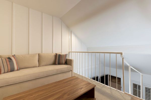 A cozy loft space with a beige sofa, striped pillows, wooden coffee table, and white railing under a sloped ceiling.