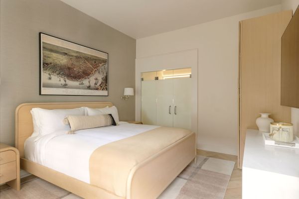 A modern bedroom with a double bed, bedside table, framed art, and a sliding door closet. Neutral tones and soft lighting complete the look.