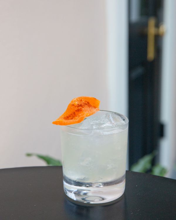 A cocktail in a glass with ice, garnished with an orange slice, sits on a black table.
