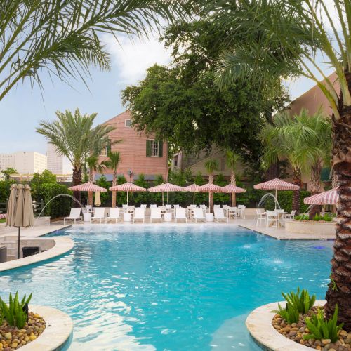 A serene pool with clear blue water, surrounded by palm trees and lounge chairs under umbrellas, creates a relaxing atmosphere.