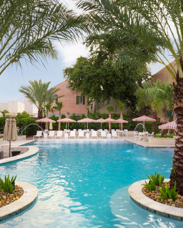 A serene pool with clear blue water, surrounded by palm trees and lounge chairs under umbrellas, creates a relaxing atmosphere.