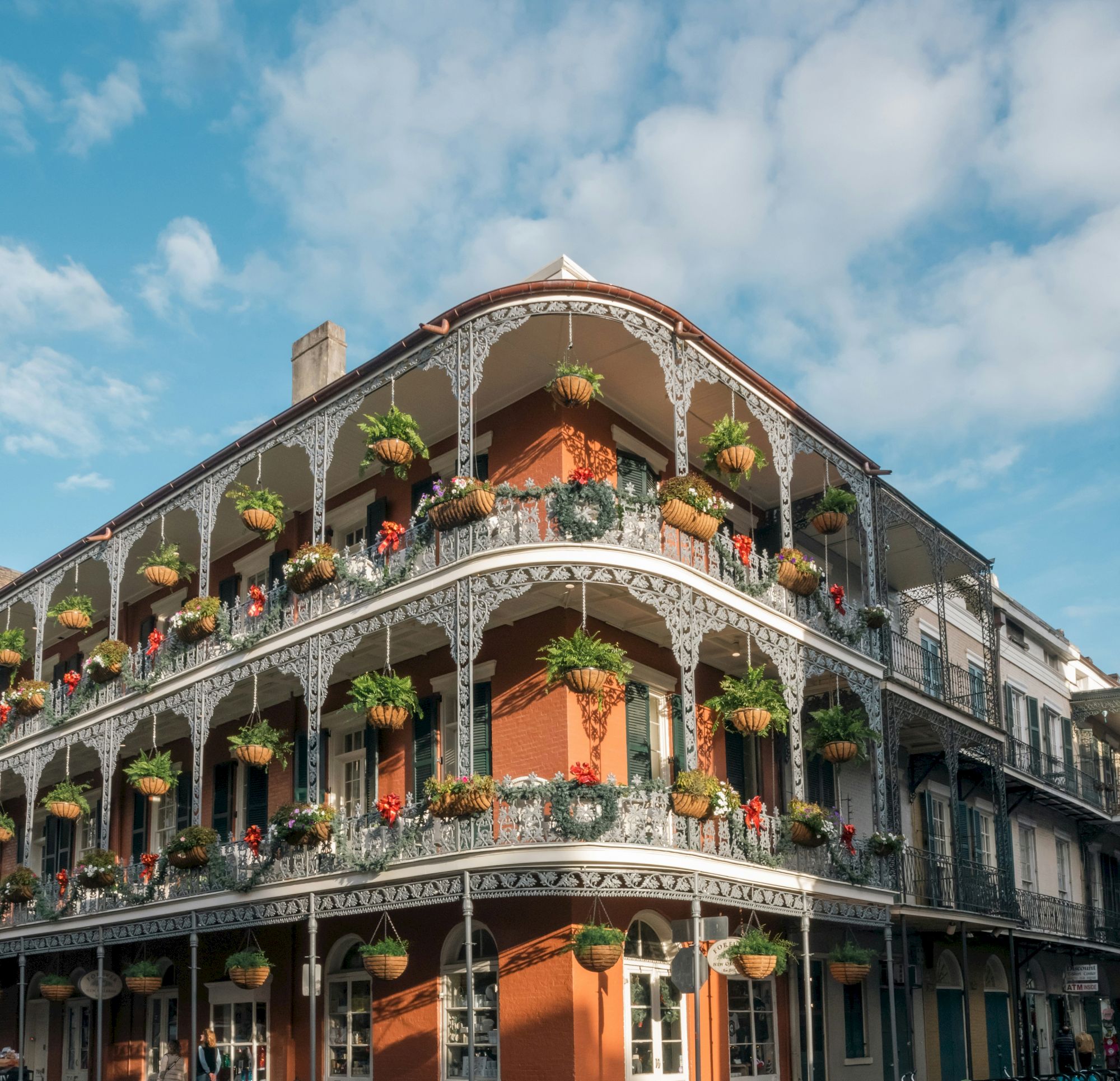 A historic building with ornate iron balconies and hanging plants, under a blue sky with clouds.