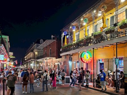 A lively street scene at night with people walking, brightly lit buildings, neon signs, and colorful balconies in a festive atmosphere.