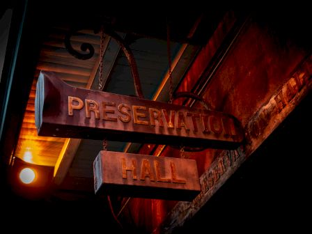 A vintage sign for "Preservation Hall" is hanging under a dim light, with a rustic background.