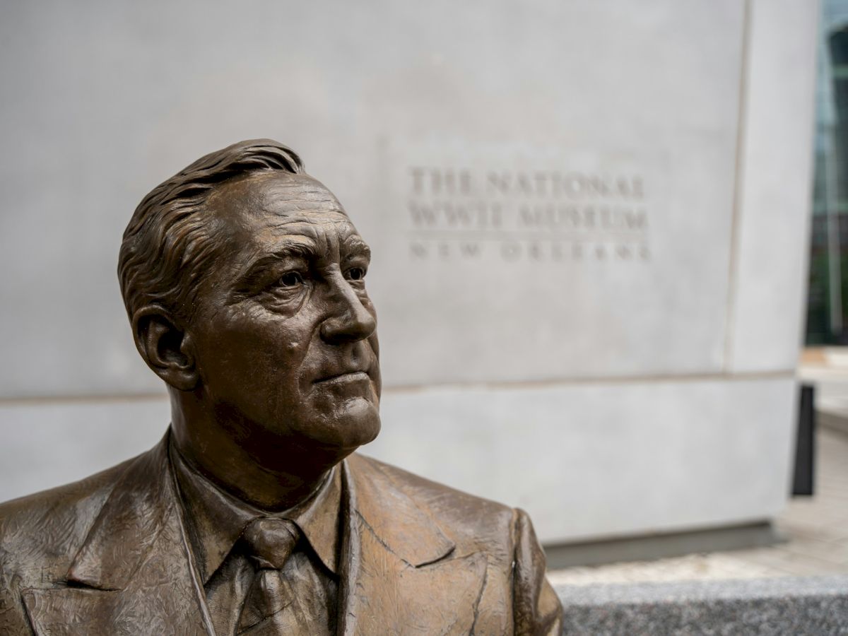 A bronze statue of a man in a suit is in front of The National WWII Museum in New Orleans.