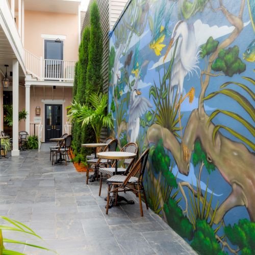 A courtyard with tables, chairs, plants, and a vibrant mural featuring birds and nature on the wall.