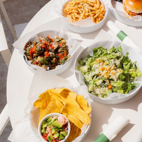 The image shows a table with a variety of food, including fries, a burger, salads, and a bowl of chips with dip.