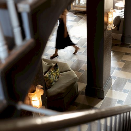 A person in motion on a tiled floor, captured from a staircase, with couches and soft lighting creating a cozy atmosphere.