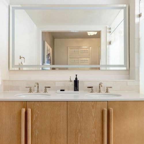 A bathroom vanity with a large mirror, dual sinks, wood cabinets, and towel on the side.
