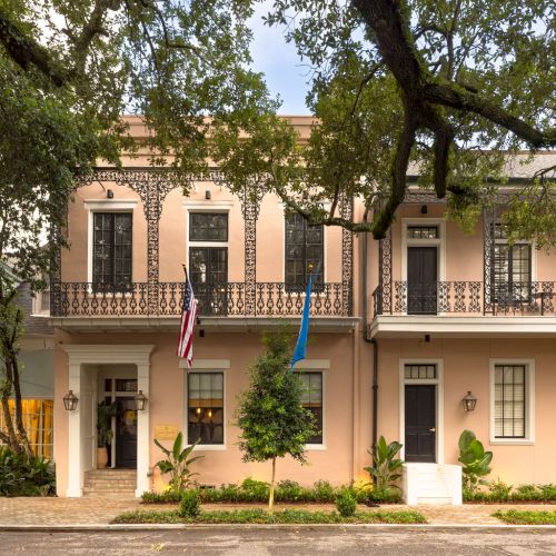 A two-story peach building with iron balconies, trees in front, and two flags displayed at the entrance.