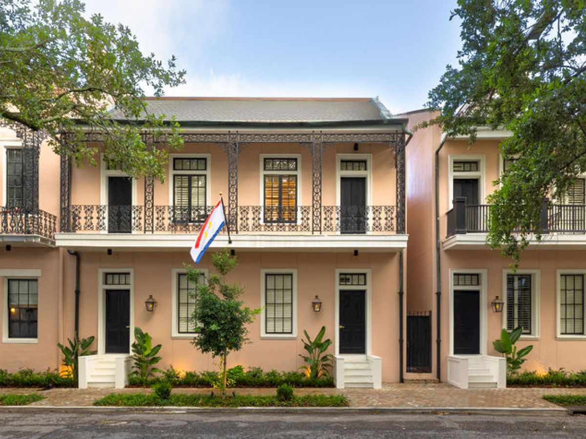 A row of elegant, two-story buildings with flags, wrought-iron balconies, and trees lining the sidewalk are shown in the image.
