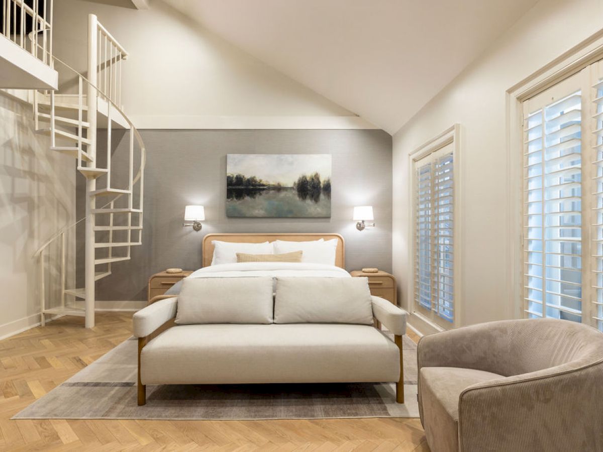 A modern bedroom with a bed, spiral staircase, armchair, and large windows with blinds. A landscape painting hangs above the bed.