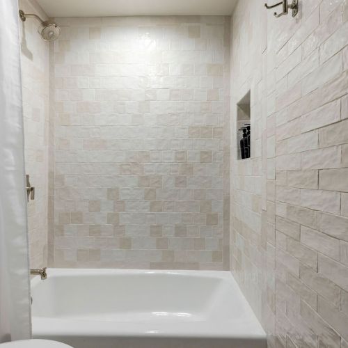 This image shows a white tiled bathroom with a bathtub, shower head, and a towel.