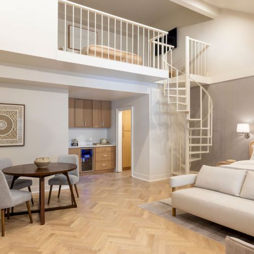 A modern loft apartment with a spiral staircase, living area, small kitchen, and dining set, featuring neutral tones and stylish decor.