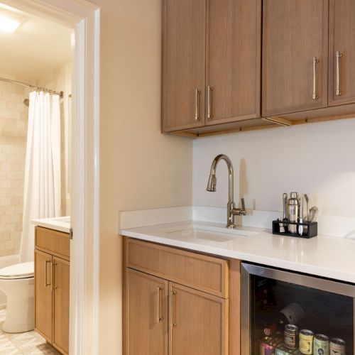 The image shows a kitchenette with wooden cabinets, a sink, and a mini-fridge; a bathroom with a toilet and shower is visible.