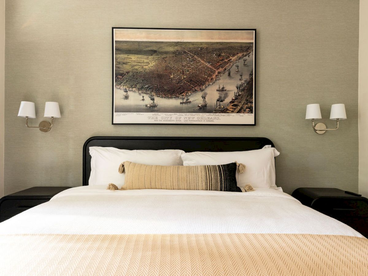 A neatly made bed with a beige and white color scheme, flanked by wall lamps, and a framed aerial view artwork above it.