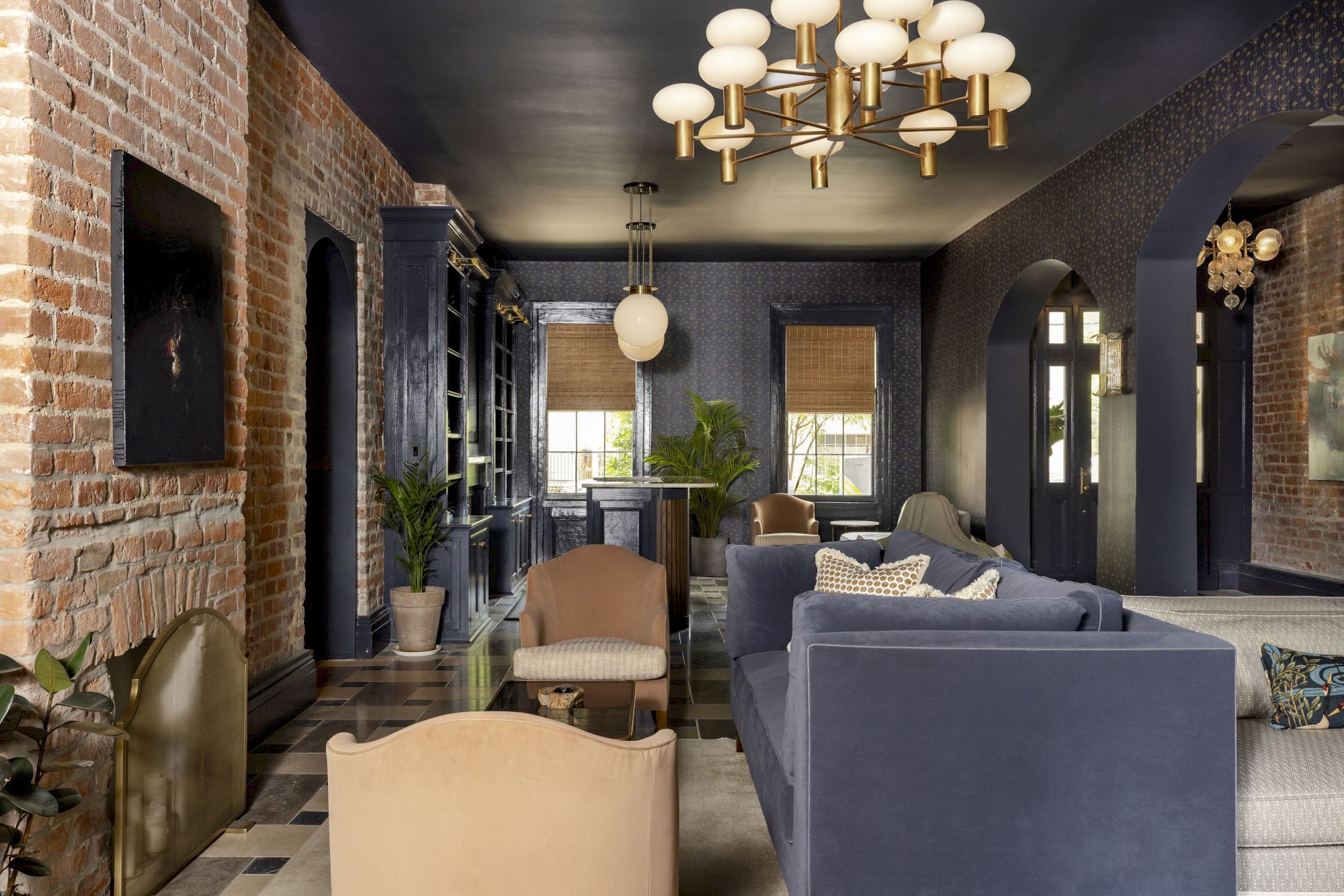 A stylish living room with navy walls, exposed brick, modern lighting, and comfortable seating, offering a cozy and elegant ambiance.