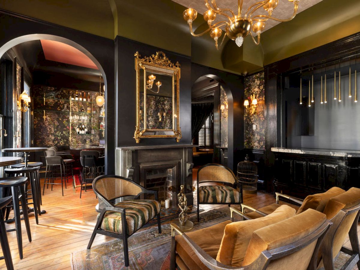 The image shows an elegant lounge with vintage decor, plush chairs, a gold-framed mirror, and dim lighting, creating a cozy atmosphere.