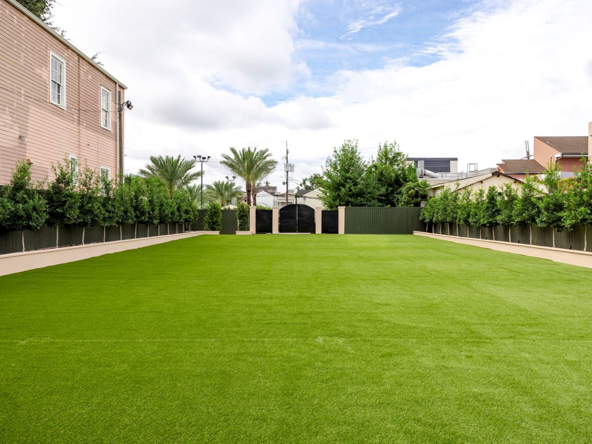 A neatly manicured lawn is surrounded by trees and a few buildings, with a clear blue sky overhead.