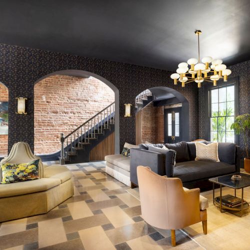 Luxurious living room with arched brick walls, checkered tile floor, modern furniture, chandelier, staircase, and abundant natural light.