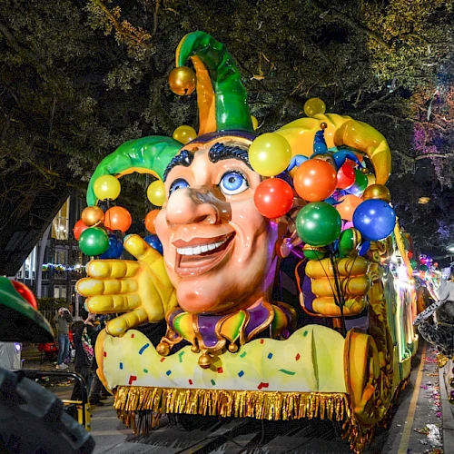 A colorful carnival float with a jester heads and balloons, parading at night with cheering crowds and a selfie moment. end.
