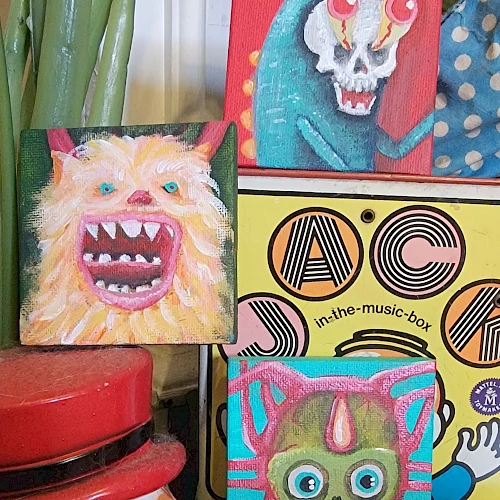 Colorful, creepy cartoon portraits on mini canvases: a chomping orange monster, a red-eyed skull, a teal demon, and a striped purple cat, all bold.