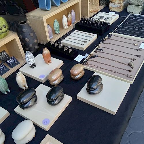 Assorted carved stone and resin animal sculptures, plus ceramic-looking pendants and keychains, displayed on trays at a shop stall.