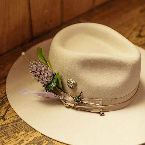 A white fedora with a decorative lavender sprig and small pins, resting on a wooden surface.