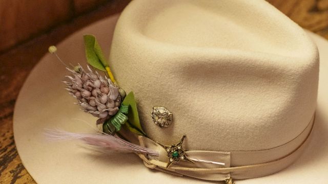 A white fedora with a decorative lavender sprig and small pins, resting on a wooden surface.