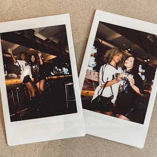Two Polaroid-style photos lie on a concrete surface, showing friends posing at a nighttime party with drinks.