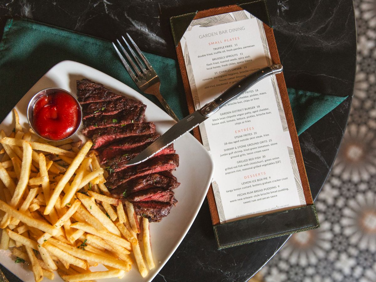 A plate of steak fries with steak and ketchup sits by a menu card listing small plates and desserts.